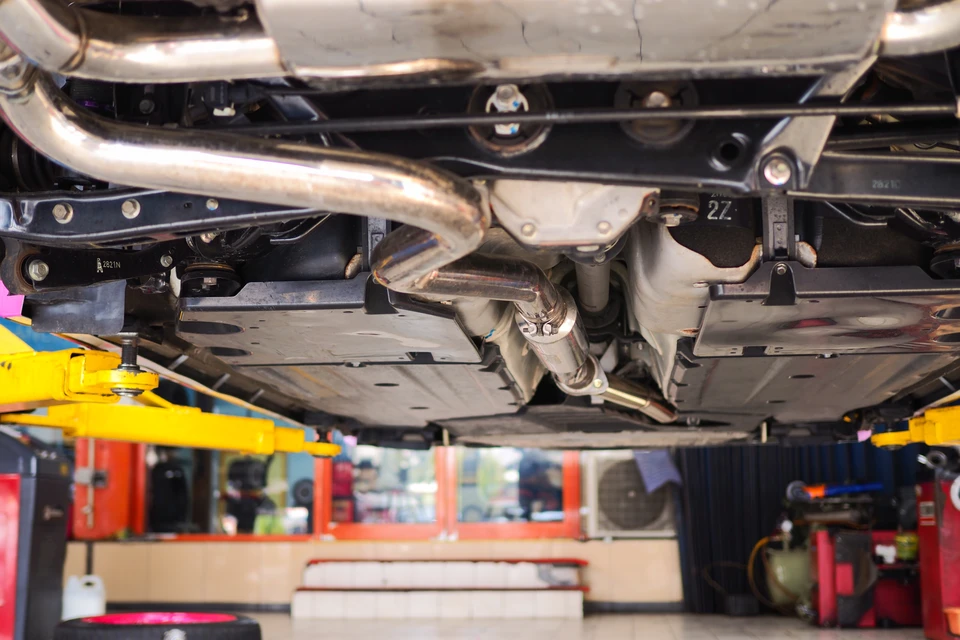 Technicien en combinaison grise et masque FFP2, agenouillé à l'arrière d'une Peugeot 3008 grise dans un garage de contrôle technique