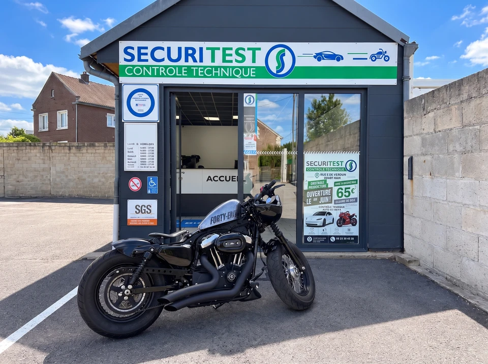 Technicien en combinaison grise et masque FFP2, agenouillé à l'arrière d'une Peugeot 3008 grise dans un garage de contrôle technique