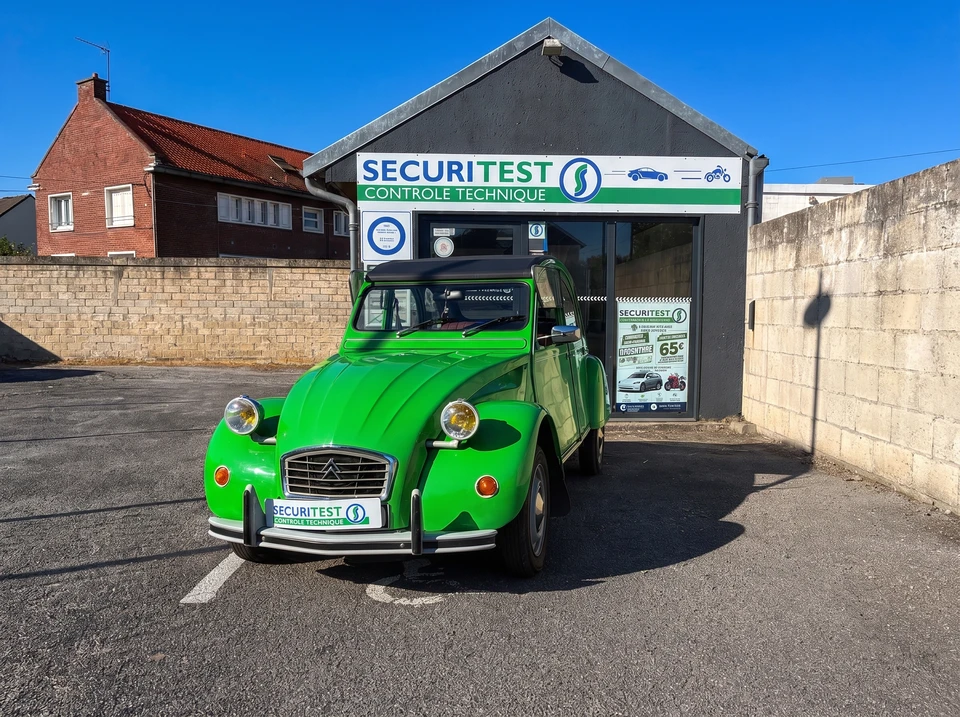 Technicien en combinaison grise et masque FFP2, agenouillé à l'arrière d'une Peugeot 3008 grise dans un garage de contrôle technique